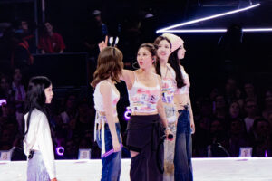 Jihyo betrachtet ein fan-gemachtes Headban, das Momo trägt - was Nayeon sehr irritiertend findet